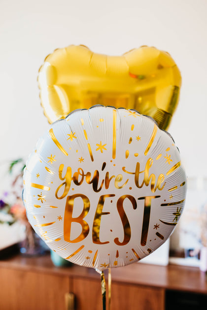 Gold and white balloon with 'you're the best' text on a blurred background