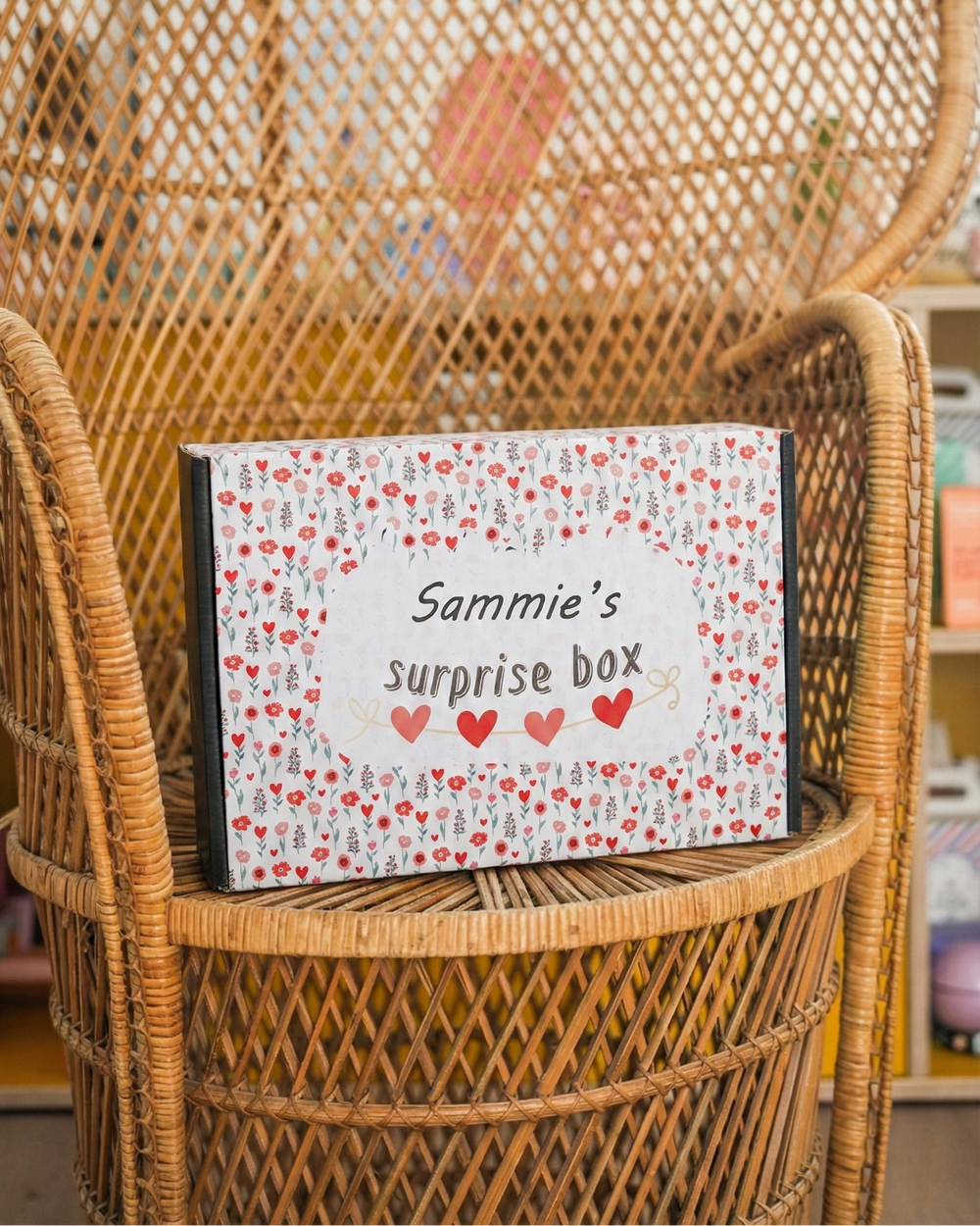 一個標有「Sammie 的驚喜盒」字樣的盒子，置於一張藤椅上，背景略顯模糊